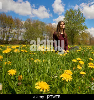 Schöne junge Frau auf einer Wiese mit vielen Löwenzahn in der Frühlingssonne. Niedrigen Winkel gedreht mit dem blauen Himmel. Stockfoto