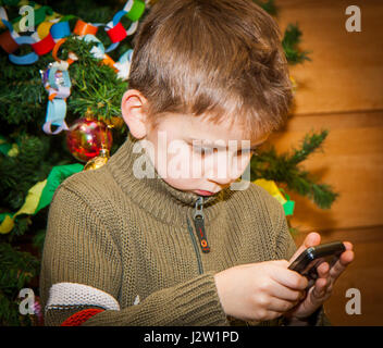 Ein kleiner blonder Junge sitzt unter einem Weihnachtsbaum und Geschenke warten. Stockfoto