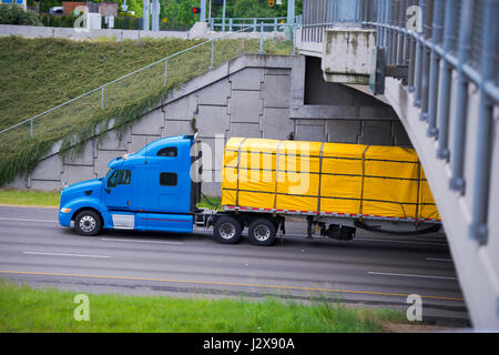 Profil von rapid leistungsstarke moderne blaue Sattelschlepper mit einem Tieflader, auf dem die Ware mit leuchtend gelbe Zelt Plane bedeckt und ziehen Sie die Gurte Stockfoto