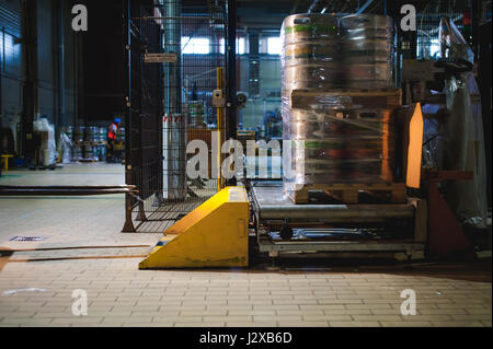 Lagermitarbeiter im Overall Kleidung, Fahrer Ausstellungsgeräte fleißig an Logistik Moving on Loader Paletten mit Bierfässer auf Linie der Fabrik für Pro Stockfoto