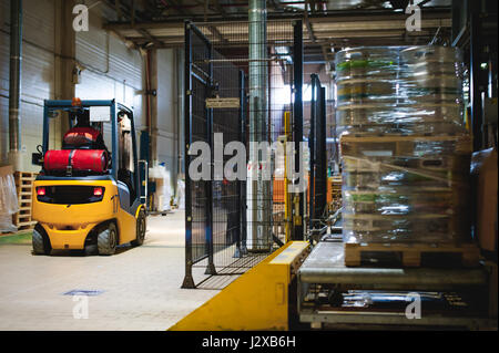 Lagermitarbeiter im Overall Kleidung, Fahrer Ausstellungsgeräte fleißig an Logistik Moving on Loader Paletten mit Bierfässer auf Linie der Fabrik für Pro Stockfoto