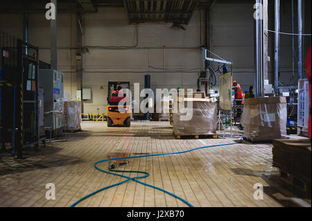 Lagermitarbeiter im Overall Kleidung, Fahrer Ausstellungsgeräte fleißig an Logistik Moving on Loader Paletten mit Bierfässer auf Linie der Fabrik für Pro Stockfoto