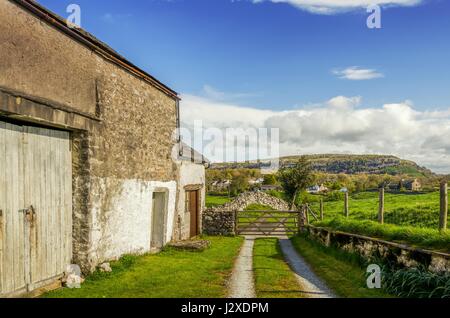 Eine alte Scheune in Cumbria an einem sonnigen Tag mit einem Holztor und entfernten Hügel. Stockfoto