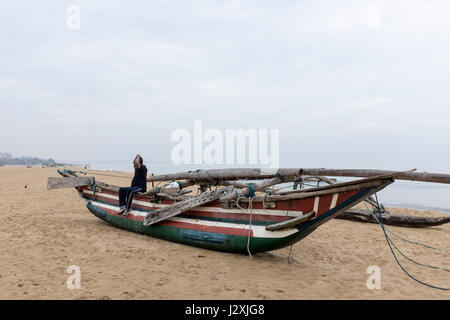 Ein Mann sitzt auf einem Traditionssegler Angelboot/Fischerboot am Strand in Negombo, Sri Lanka. Stockfoto