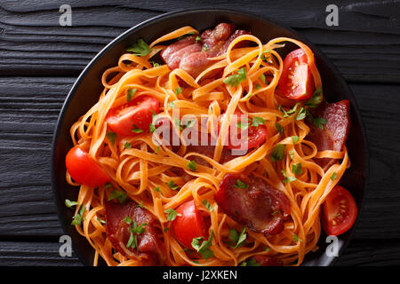 Karotten-Nudeln mit gebratenem Speck, Greens und Tomaten Nahaufnahme auf einem Teller auf den Tisch. Horizontale Ansicht von oben Stockfoto