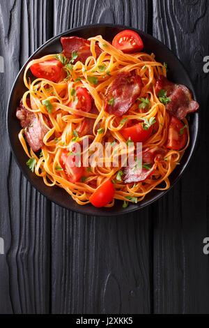 Karotten-Nudeln mit Speck und Tomaten Nahaufnahme auf einer Platte. Vertikale Ansicht von oben Stockfoto