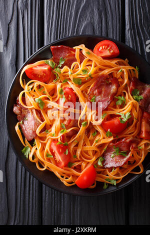 Karotten-Nudeln mit gebratenem Speck, Greens und Tomaten Nahaufnahme auf einem Teller auf den Tisch. Vertikale Ansicht von oben Stockfoto