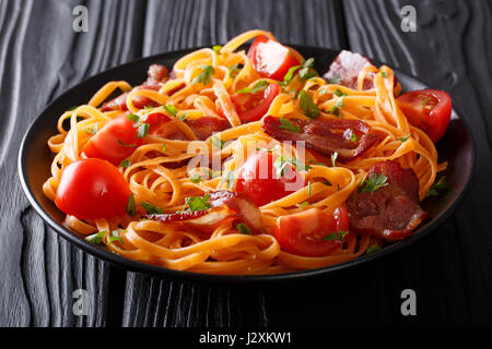 Italienische Orangen Pasta mit gebratenem Speck, Greens und frischen Tomaten Nahaufnahme auf einem Teller auf den Tisch. horizontale Stockfoto