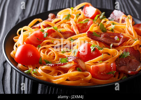 Karotten-Nudeln mit gebratenem Speck, Greens und Tomaten Nahaufnahme auf einem Teller auf den Tisch. horizontale Stockfoto