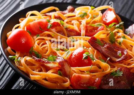 Karotten-Nudeln mit gebratenem Speck und Tomaten Closeup auf einem Teller auf den Tisch. horizontale Stockfoto