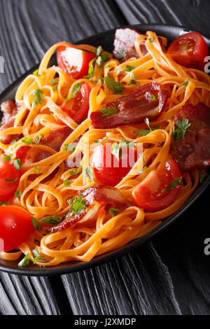 Karotten-Nudeln mit Speck und Tomaten Nahaufnahme auf einem Teller auf den Tisch. vertikale Stockfoto