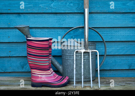 Gummistiefel und Gartengeräte auf blauem Hintergrund Stockfoto