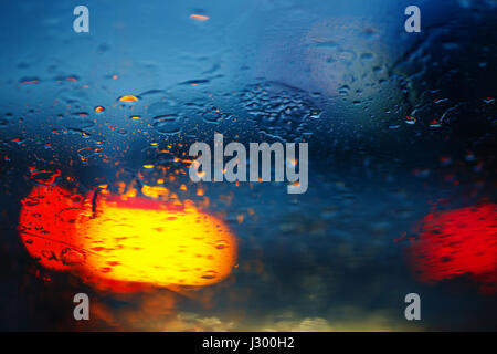 Regentropfen auf Autoglaserei mit Ampel, Fokus auf Regentropfen Stockfoto