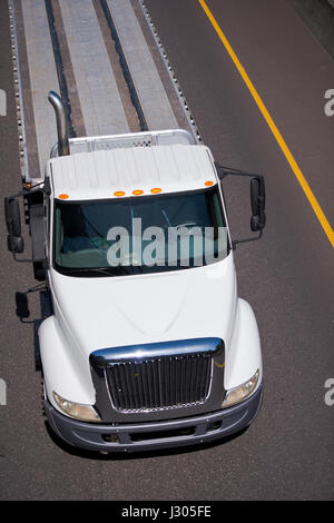 Weißer moderner Mittelklasse-Lastkraftwagen für den lokalen Transport Fracht mit Flachbett Anhänger auf der Autobahn auf einem Hintergrund aus grauem Asphalt Stockfoto