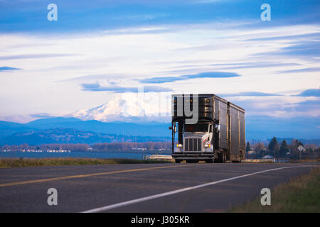 Stilvolle klassische weiße LKW mit einer großen hoch schwarz überdachte Anhänger für den Transport von Luxus und exotische Autos auf der Panoramastraße mit Berggipfeln Stockfoto