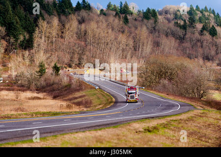 Klassische big Rig Sattelschlepper mit den Attributen der einzelnen Design- und LKW Zubehör Transport von Ladung auf einer kurvenreichen Straße, umgeben von Hügeln Stockfoto