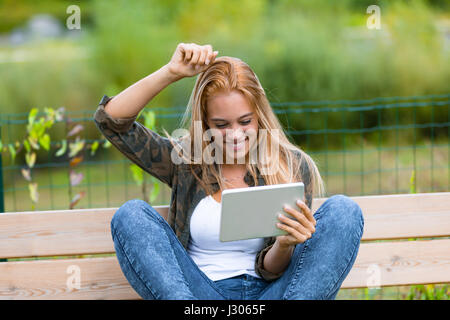 Mädchen steigt er Schaden weil sie erfolgreich oder zu gewinnen ist oder einfach auf um den Kopf zu kratzen, ist sie etwas auf ihre digitale Tablet im freien lesen Stockfoto