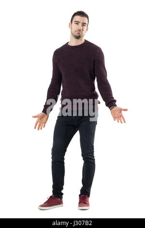 Lächelnd verwirrten Mann mit braunen Pullover mit Ausbreitung Armen nachschlagen. Ganzkörper-Länge-Porträt über weiße Studio-Hintergrund isoliert. Stockfoto