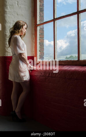 Einsame Reife Frau am Fenster stehend Stockfoto