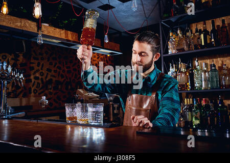 Das Barkeeper mit einem Bart gießt Alkohol in Gläser in einer bar Stockfoto