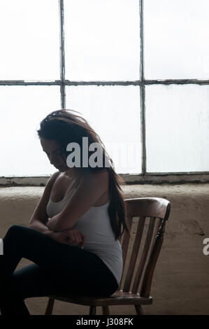 Traurige junge Frau saß auf einem Stuhl am Fenster Stockfoto