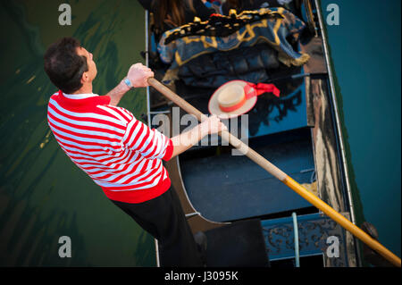 Venedig - 23. April 2013: Venezianischen Gondoliere im traditionellen rot und weiß gestreiften Hemd flache seine Gondel unter einer Brücke. Stockfoto