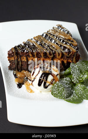 Mohn-Kuchen mit Eis und grüne Minze. Dessert. Stück Kuchen lecker Mohn auf weißen Teller auf dunklem Hintergrund. Stockfoto