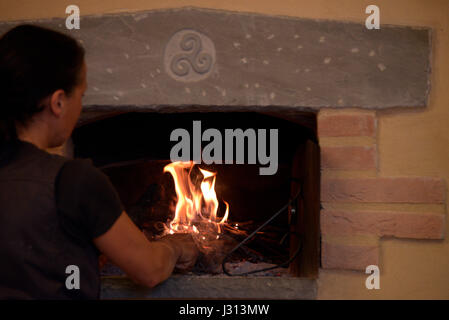 Frau stellt sich auf das Feuer von einem Holzofen Stockfoto