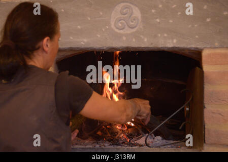 Frau stellt sich auf das Feuer von einem Holzofen Stockfoto