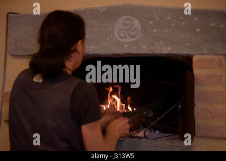 Frau stellt sich auf das Feuer von einem Holzofen Stockfoto