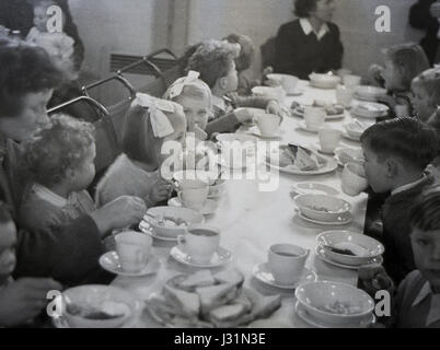 1950s, historisch, eine Teeparty für Kinder, in einem Dorfsaal sitzen junge Jungen und Mädchen an einem langen Tisch mit einer Tischdecke und genießen Tee und Sandwiches, England, Großbritannien. Stockfoto