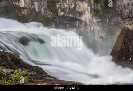 Menschen stehen auf einer Plattform am Rheinfall in Neuhausen bin Rheinfall, Schweiz, 23. April 2017. Der Rheinfall ist der größte schlicht Wasserfall in Europa. Foto: Lino Mirgeler/dpa Stockfoto