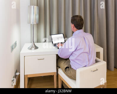 Senior Geschäftsmann in Hotelzimmer am weißen Tisch Schreibtisch arbeiten auf seinem Laptop in der Nachtsitzung Stockfoto