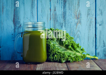 eine Grünkohl-Smoothie, serviert in einem Glas Mason und ein Blatt von Kale auf eine Holzoberfläche vor einem blauen rustikalen hölzernen Hintergrund Stockfoto