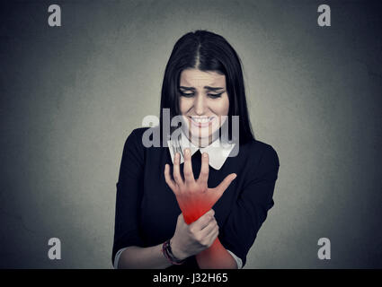 Junge Frau mit ihrem schmerzhafte Handgelenk auf graue Wand Hintergrund isoliert rot gefärbt. Verstauchung-Schmerzen Stockfoto