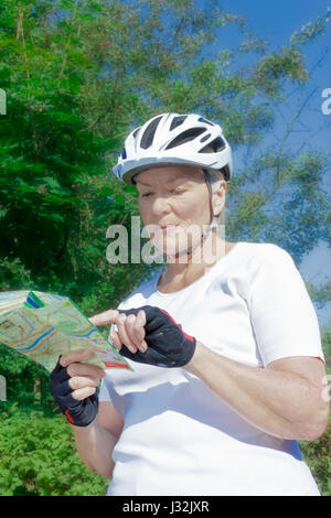 Ältere Frau im Freien im Sommer Sonne mit Fahrrad Helm, Handschuhe, weißes T-Shirt und Karte, immer eine schöne Bräune und ausreichend Vitamin D Stockfoto