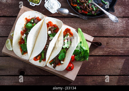 mexikanische Steak und Chicken Fajitas in gusseisernen Pfanne oben abgeschossen mit Mais-tortillas Stockfoto