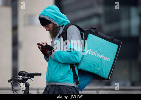 Ein Deliveroo Arbeiter auf einem Fahrrad mit einem Delivroo Marken-Rucksack mit Speisen zum mitnehmen. Stockfoto