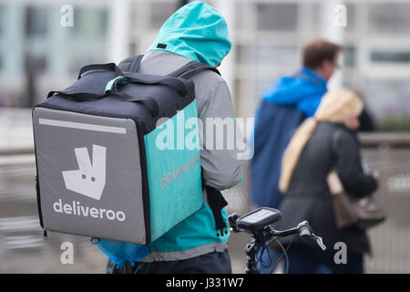 Ein Deliveroo Arbeiter auf einem Fahrrad mit einem Delivroo Marken-Rucksack mit Speisen zum mitnehmen. Stockfoto