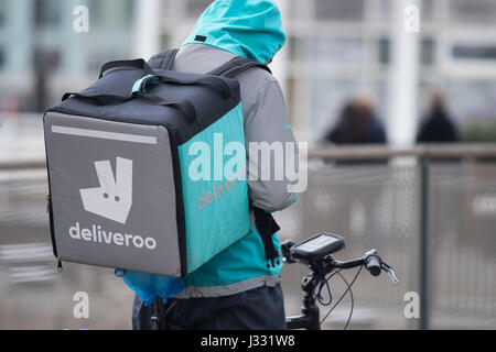 Ein Deliveroo Arbeiter auf einem Fahrrad mit einem Delivroo Marken-Rucksack mit Speisen zum mitnehmen. Stockfoto