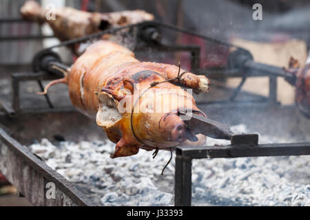 Traditionell Spanferkel auf einer sich drehenden Spieß mit Feuer und Rauch. Sehr leckeres Essen. Stockfoto