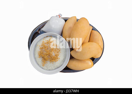 Draufsicht der isolierten Dessert süße Gelbe Mango und Kokosmilch in Tasche auf Teller mit Klebreis durch Geröstete Sojabohnen in weiße Schüssel abgedeckt. Stockfoto