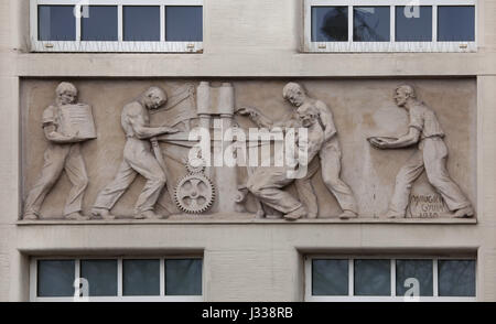 Unfall in der Druckerei. Relief von dem ungarischen Bildhauer Gyula Maugsch (1930) am Nordflügel des Art-Déco-Gebäudes von Budapest Arbeitnehmer Krankenkasse in Budapest, Ungarn. Das Gebäude, nun als Sitz der nationalen Sozialversicherung Zentrum (OTI), wurde von ungarischen Architekten Marcell Komor und Dezsö Jakab entworfen und im Jahre 1913 gebaut. Der Nordflügel wurde vom Architekten Aladar Sos 1930-1931 hinzugefügt. Stockfoto