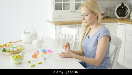 Junge schöne Blondine in casual-Outfit sitzt am Tisch an Küche und Ostereier für Ostern. Stockfoto