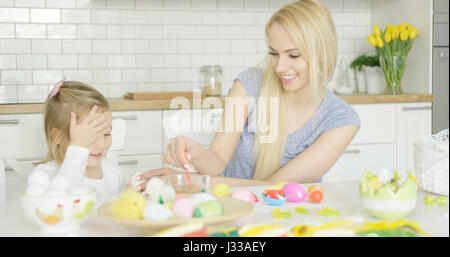 Lachen, junge Mutter und wenig liebenswert Mädchen Ostereier färben zusammen sitzend am Tisch in der Küche. Stockfoto
