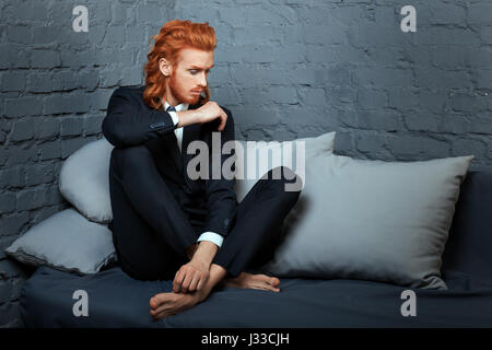 Metrosexuellen Mann mit roten Haaren und Bart auf einer Couch sitzend. Stockfoto