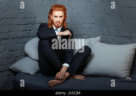 Der Mann mit den roten Haaren und Bart, auf dem Sofa sitzen. Sommersprossen im Gesicht. Stockfoto