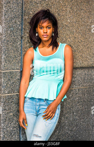 Einsames Mädchen. Tragen grüne Tank-Top, modische Jeans, Ohrringe, junge afroamerikanische Frau gegen die Wand in New York, traurig, zu denken, Stockfoto