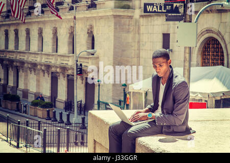 Young African American Mann Reisen, arbeitet in New York, sitzen auf der Straße von Vintage Büro Gebäude, lesen, arbeiten am Laptop-Computer. Wand-Str Stockfoto