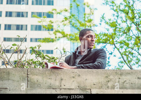 Afrikanische amerikanische Studentin Standby Wand außerhalb Büro Gebäude auf dem Campus in New York, Buch zu lesen, schaut sich um, warten auf Sie. Stockfoto